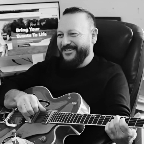 Image of dark-haired bearded man sitting down playing the guitar. Rick Navarro - Director of SEO and Website Design, NAVARRO CREATIVE GROUP, LLC. Digital Marketing Professionals in Nashville