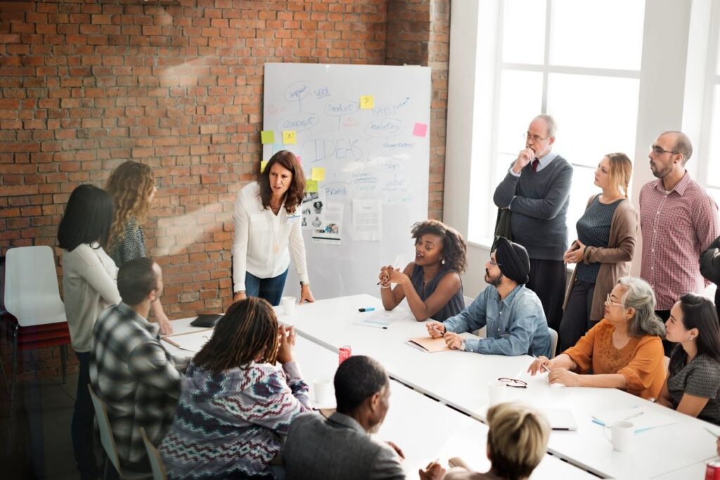 Small group of professionals in discussion around white board and boardroom table. AI vs Humans - Marketing Today, Navarro Creative Group, Nashville Hendersonville TN Marketing Agency.